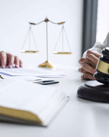 Balance de la justice, marteau de juge, et documents sur un bureau. Décisions juridiques, droit et justice. Mains croisées en arrière plan.