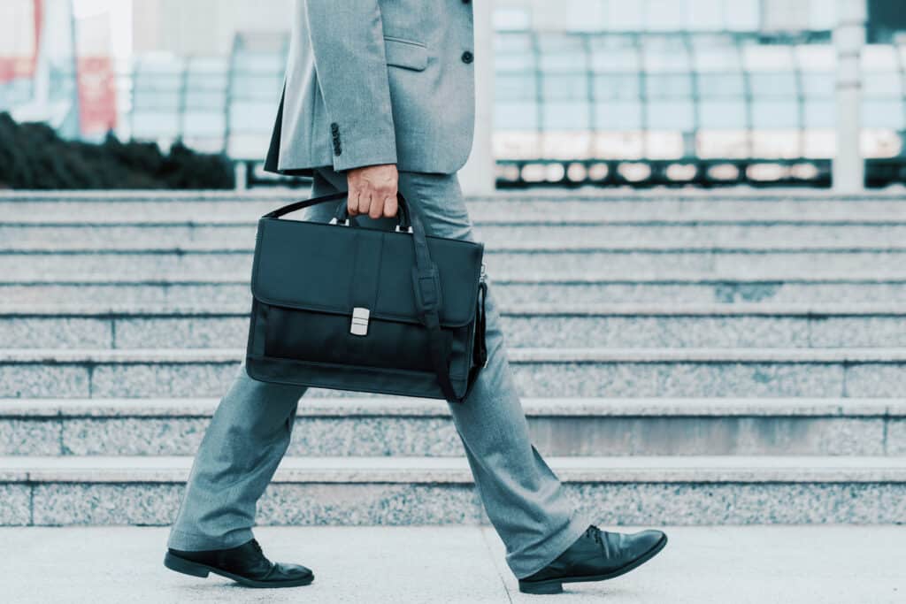 Homme en costume gris marchant sur des marches en pierre, portant un attaché-case noir à la main. Business et déplacement urbain.