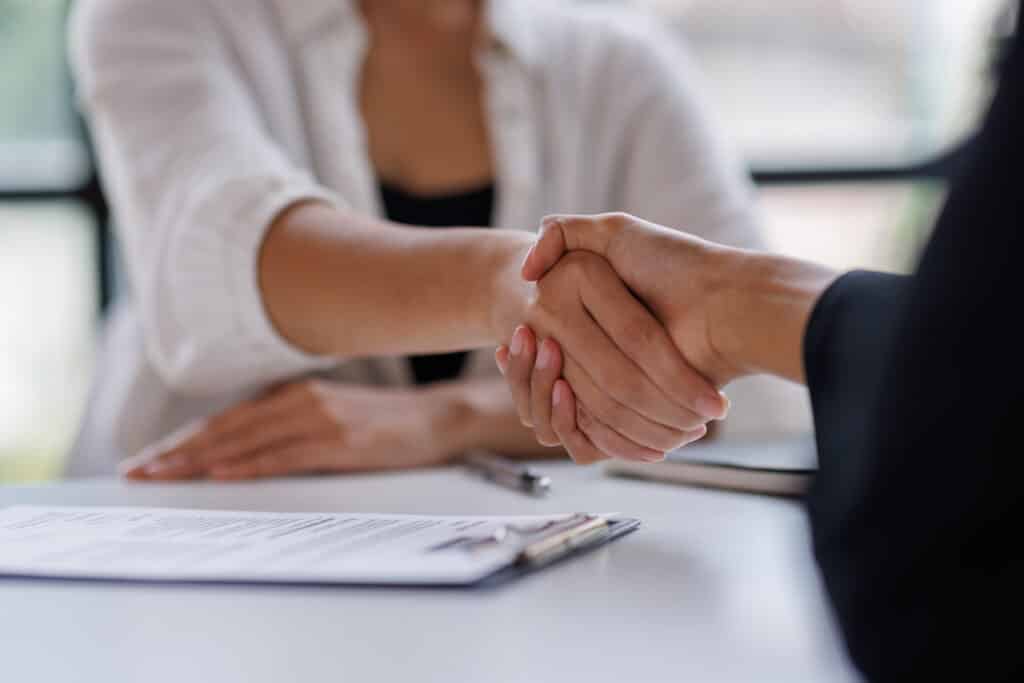 Poignée de main entre deux personnes au-dessus d'un contrat, scellant un accord ou un partenariat d'affaires.