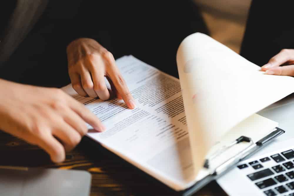 Mains pointant du doigt sur un document pendant une réunion de travail. Collaboration et lecture de contrat ou rapport.